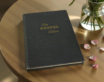 May include: A dark blue book titled "The Gospel Choir" with gold lettering, resting on a round wooden table. A small glass vase with white flowers and greenery sits nearby, with scattered pink petals.