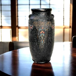 May include: A black ceramic vase with a textured surface and ornate, colorful geometric patterns. The vase has two small handles and a wide opening. The design includes red, blue, and gold accents.
