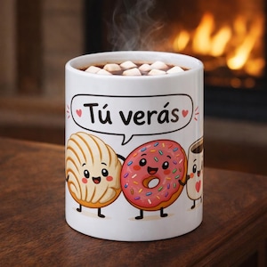 May include: White ceramic mug filled with hot chocolate and marshmallows. The mug features cartoon illustrations of a concha, a donut, and a coffee cup, with the text "Tú verás" in a speech bubble. Steam rises from the drink.