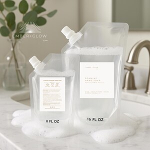 May include: Two clear plastic pouches of foaming hand soap, one labeled 8 fl oz and the other 16 fl oz. The pouches have white spouts and labels with text. The soap is surrounded by white foam, with a sink and faucet in the background.