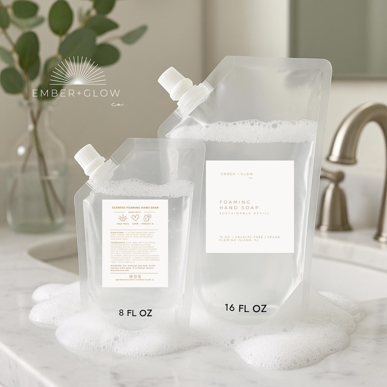 May include: Two clear plastic pouches of foaming hand soap, one labeled 8 fl oz and the other 16 fl oz. The pouches have white spouts and labels with text. The soap is surrounded by white foam, with a sink and faucet in the background.