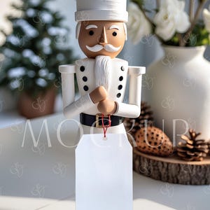 May include: A wooden nutcracker figurine in a white uniform with black buttons and a black belt. The figurine has a white mustache and a blank white tag hanging from its hands. The background includes a vase of white flowers and pine cones.