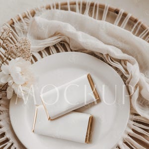 Pode incluir: Duas barras de chocolate branco com embalagens de folha de ouro em um prato branco. O prato está em um tapete de palha trançado com uma toalha de tecido branco.