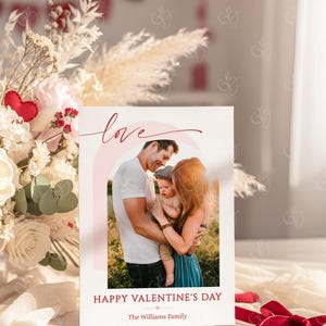 May include: A Valentine's Day card featuring a family portrait with a soft, warm color palette. The word "love" is written in cursive above the photo, and "Happy Valentine's Day" is printed below. The family is embracing, with a soft pink rainbow arching behind them.