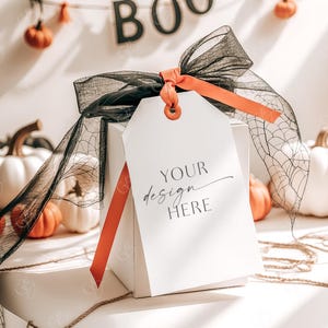 May include: A white gift box with a black and orange ribbon and a tag that says "YOUR design HERE". The box is surrounded by small white pumpkins and a string of orange pumpkins with a "BOO" banner.