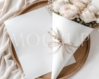 Puede incluir: Una maqueta de tarjeta blanca en una bandeja de madera con un ramo de rosas blancas envuelto en papel blanco y atado con cuerda.