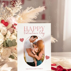 May include: A Valentine's Day card with a family photo inside an oval frame. The card reads "HAPPY Valentines Day" in pink script, with two pink heart balloons. The family name "THE WILLIAMS FAMILY" is printed at the bottom.