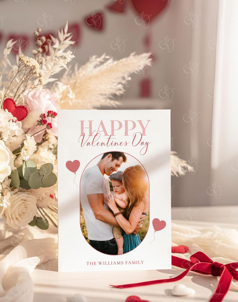 May include: A Valentine's Day card with a family photo inside an oval frame. The card reads "HAPPY Valentines Day" in pink script, with two pink heart balloons. The family name "THE WILLIAMS FAMILY" is printed at the bottom.