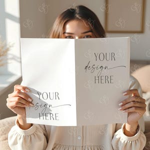 May include: A person holding a folded card with the text "YOUR design HERE" in a script font. The card is white on one side and off-white on the other. The person is wearing a beige dress.