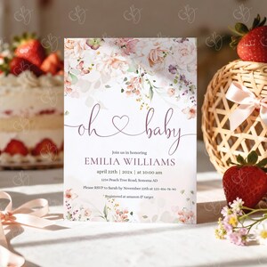 May include: A baby shower invitation with floral accents and the words "oh baby" in cursive. The invitation includes details for Emilia Williams' baby shower, including the date, time, and location. Strawberries and a cake are in the background.