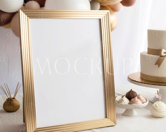May include: A gold rectangular picture frame with a white interior, leaning against a white surface. The word "MOCKUP" is faintly visible on the frame. Balloons and a small cake are in the background, suggesting a celebratory theme.