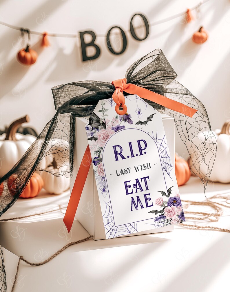 May include: A white gift tag with a purple floral design and a black spider web. The tag has the text "RIP - Last Wish - Eat Me" in purple lettering.