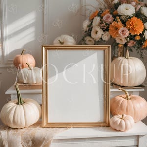May include: A gold framed mockup with a white interior, surrounded by pumpkins in shades of white and peach. A floral arrangement with orange and white flowers sits in the background. The scene is set on a white dresser.