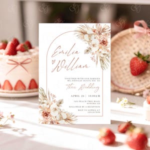 May include: Wedding invitation with the names "Emilia William" in elegant script, framed by floral arrangements in soft peach and cream tones. The invitation includes the wedding date, time, and location details.