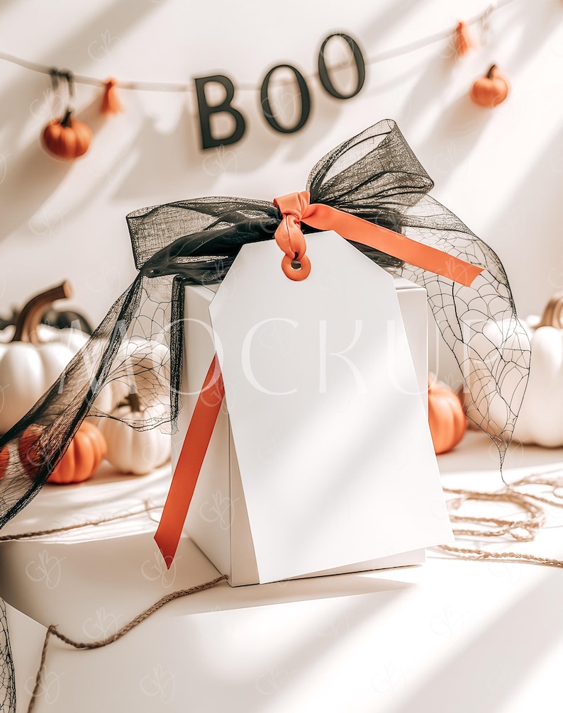 May include: A white gift box with a black and orange ribbon and a blank gift tag. The box is surrounded by small orange pumpkins and a black spiderweb. The background has a banner that says "BOO" in black letters.