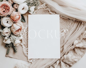 Può includere: Una carta bianca con la parola "MOCKUP" in testo grigio chiaro, circondata da un bouquet di rose rosa e bianche e verde. La carta poggia su un centrino di pizzo beige e tessuto drappeggiato.