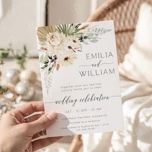 May include: A white wedding invitation with floral watercolor design. The invitation features the names "EMILIA and WILLIAM" and the words "wedding celebration". The date and time are also included.