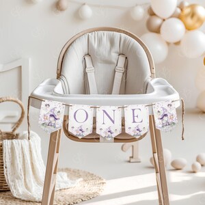 May include: A white high chair with a purple and white banner that says "ONE" with a fairy theme. The banner has images of fairies, mushrooms, and flowers.