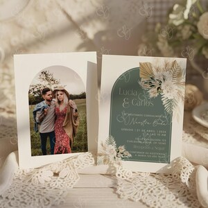 K&ouml;nnte beinhalten: Zwei Hochzeitseinladungskarten. Eine Karte zeigt ein Foto eines Paares in einem Torbogen. Die andere Karte hat Text auf Spanisch, mit einem tealfarbenen Hintergrund und floralen Akzenten. Die Karten liegen auf einer wei&szlig;en Oberfl&auml;che mit Spitzenbesatz.