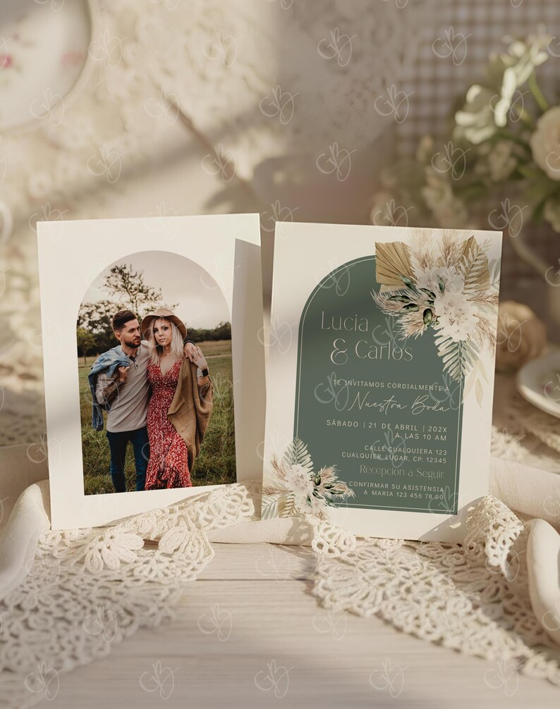 K&ouml;nnte beinhalten: Zwei Hochzeitseinladungskarten. Eine Karte zeigt ein Foto eines Paares in einem Torbogen. Die andere Karte hat Text auf Spanisch, mit einem tealfarbenen Hintergrund und floralen Akzenten. Die Karten liegen auf einer wei&szlig;en Oberfl&auml;che mit Spitzenbesatz.