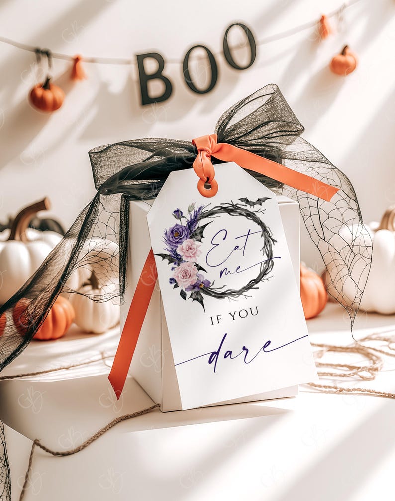 May include: A white gift box with a black and purple floral wreath with bats and the text "Eat me if you dare" on a white tag tied with a black and orange ribbon.