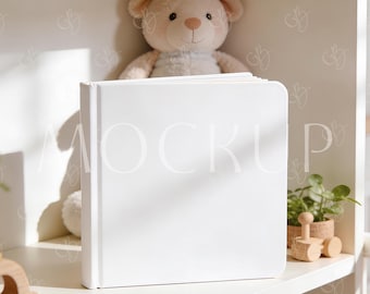 以下が含まれることがあります： 白い棚に置かれた、表紙に「MOCKUP」と書かれた白い本。本の後ろにはテディベアが座っています。棚には、小さな鉢植えの植物や木製のおもちゃの車など、他のアイテムも置かれています。