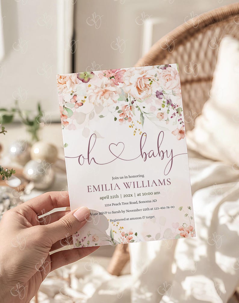 May include: A baby shower invitation with floral accents in pink and peach tones. The text "oh baby" is written in a delicate script, with event details below. The invitation is held in a hand.