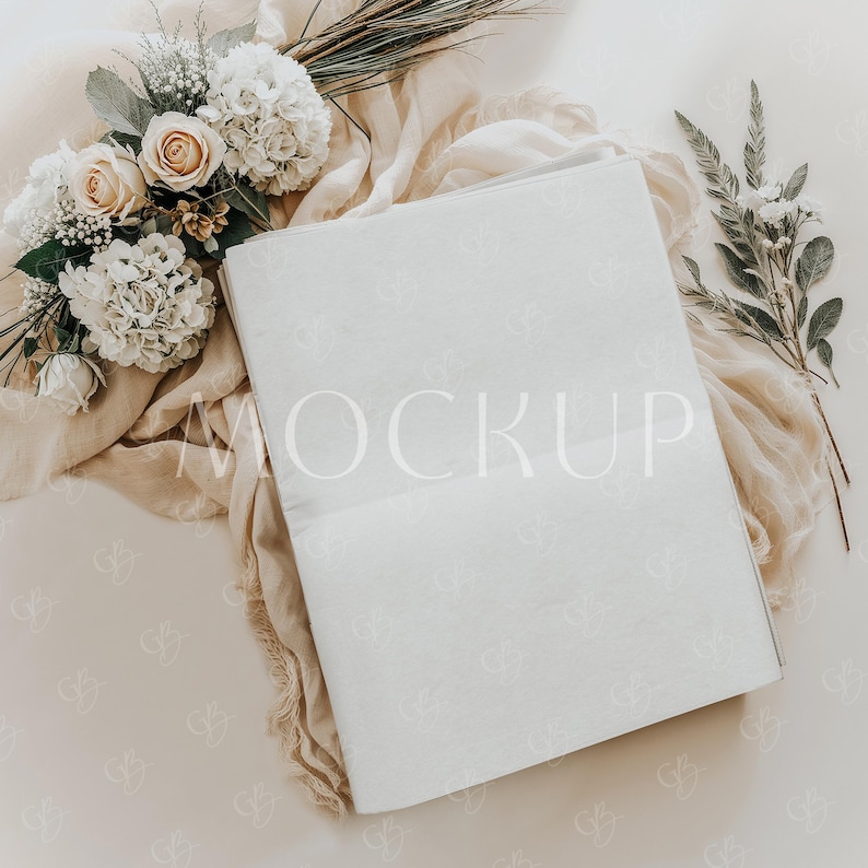 Puede incluir: Una maqueta de tarjeta blanca con la palabra "MOCKUP" impresa en blanco en la tarjeta. La tarjeta est&aacute; sobre una tela beige con flores blancas y hojas verdes.