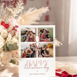 May include: A Valentine's Day card with the word "LOVE" in large pink letters and family photos. The card reads "HAPPY Valentine's day" and "The Williams Family" in a script font. A red ribbon and floral arrangement are in the background.