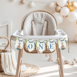 May include: A white high chair with a blue and green banner that says "ONE" with a globe and airplane design. The banner is strung across the front of the high chair.