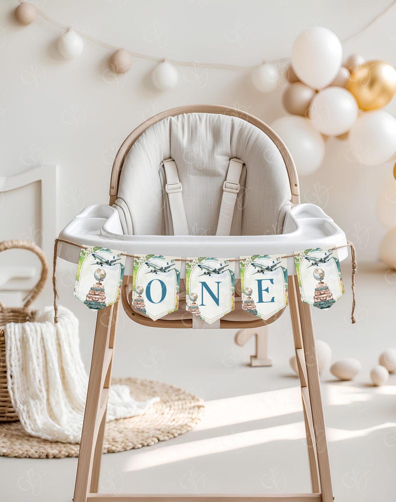 May include: A white high chair with a blue and green banner that says "ONE" with a globe and airplane design. The banner is strung across the front of the high chair.