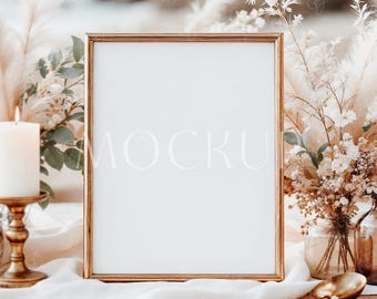 May include: A gold framed sign with the word "MOCKUP" in white letters. The sign is surrounded by floral arrangements, a lit candle, and a gold spoon. The background is blurred, suggesting a beach setting.