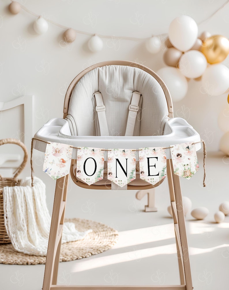 May include: A white high chair with a floral banner that says "ONE" hanging from it. The banner has a pink, green, and white floral pattern with a small fairy illustration on each flag.
