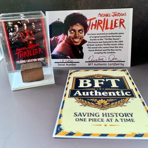 May include: An authentic piece of wood from the "Thriller House" in a clear display case, with a certificate featuring Michael Jackson. The certificate states the wood is from the 1983 music video. A BFT Authentic certificate is also present.