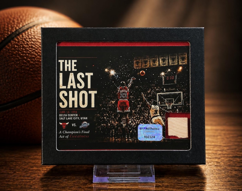 May include: A framed sports collectible titled The Last Shot featuring Michael Jordan in a red jersey, a basketball court scene, the text June 14 1998 Delta Center Salt Lake City Utah, a Bulls and Jazz logo, and a small wood piece with a holographic sticker.