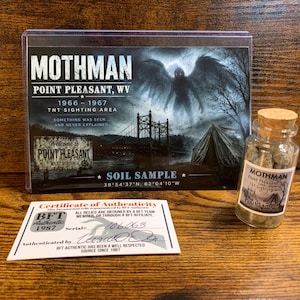 Op de afbeelding: Een Mothman bodemmonsterkit met een displaykaart met een illustratie van een gevleugeld wezen, een glazen flesje met een kurkstop met aarde, en een wit certificaat van echtheid met het BFT Authentic 1987 logo en serienummer 106063.