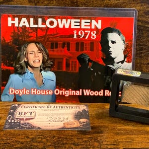 May include: A rectangular display card featuring the text HALLOWEEN 1978 and Doyle House Original Wood Relic, showing a film scene with a person and a masked figure. Includes a Certificate of Authenticity and a small wood piece in a black frame.
