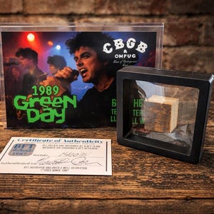 Può includere: Una foto incorniciata del concerto dei Green Day del 1989, con il nome della band in verde. Un piccolo blocco di legno incapsulato è esposto accanto alla foto. È presente anche un certificato di autenticità.