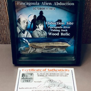 May include: A framed display with a wood relic from the Pascagoula Alien Abduction site, October 11, 1973. The display includes images and text about the event, with a certificate of authenticity from BFT Authentic.