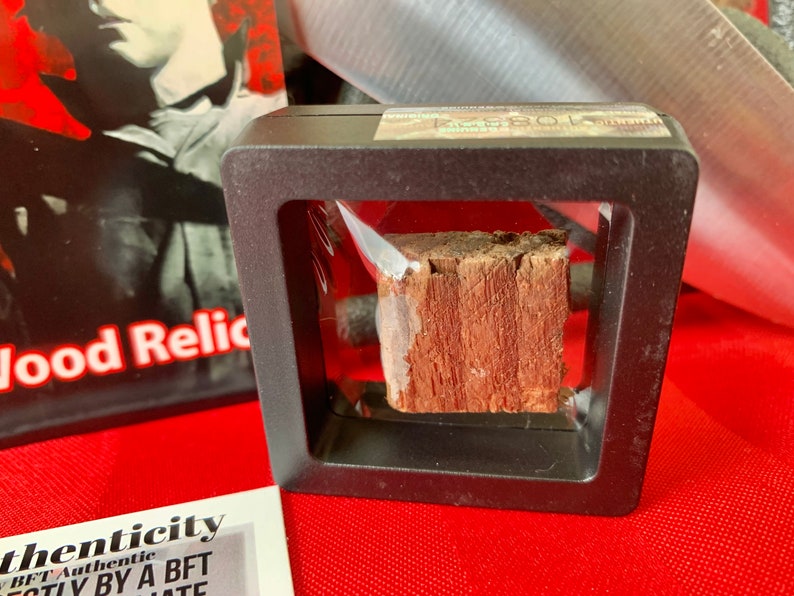 Pu&ograve; includere: Un piccolo pezzo di legno racchiuso in una teca di plastica nera con un coperchio di plastica trasparente. Il legno &egrave; di colore marrone rossiccio e ha una consistenza ruvida. La teca ha un'etichetta che dice "Reliquia di legno autentica".