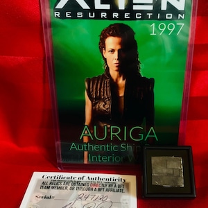 May include: A certificate of authenticity for a piece of the "Auriga" ship from the movie "Alien Resurrection". The certificate is signed by "Michael Ovitz" and has a serial number of "247120".