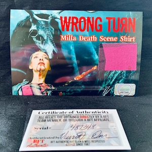 May include: A certificate of authenticity for a piece of clothing from the movie "Wrong Turn". The certificate is pink and white with black text. The text reads "Wrong Turn Milla Death Scene Shirt". The certificate has a serial number of 487348 and is authenticated by Don. The certificate is from BFT Authentic, a well-respected source since 1987.