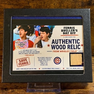 May include: Framed "Ferris Bueller's Day Off" authentic wood relic from Wrigley Field. The framed piece includes a small piece of original wood seat, movie title, and text. The frame is black.