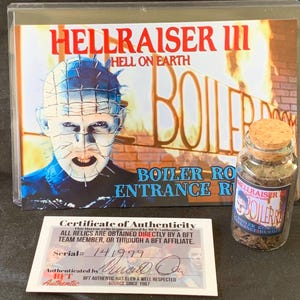 Może przedstawiać: Plakat filmu Hellraiser III z napisem "Hell on Earth" i "Boiler Room Entrance". Mały szklany słoik z korkiem i etykietą z napisem "Hellraiser Boiler Room". Dołączony jest również certyfikat autentyczności.