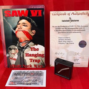 May include: A certificate of authenticity for a piece of neck wire used in the Saw VI film. The certificate is signed by the producers of the film and includes a photo of the wire in a black display case. The text on the certificate reads "Piece of Allen's (Shawn Ahmed) Neck Wire Used in Hanging Trap Scene".