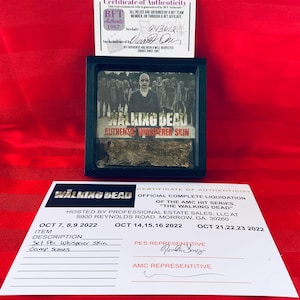 Puede incluir: Un certificado de autenticidad para un accesorio de The Walking Dead, una pieza de utilería de piel de Whisperer de la serie de televisión. El certificado proviene de una venta de bienes raíces profesional e incluye las fechas de la venta. El accesorio se muestra en un marco negro con una imagen de los Whisperers de la serie.