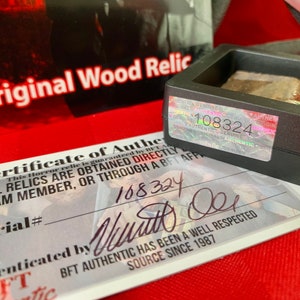Pu&ograve; includere: Un certificato di autenticit&agrave; bianco con un bordo nero e il testo "Certificate of Authenticity" in nero. Il certificato ha un numero di serie, una firma e il testo "BFT Authentic has been a well respected source since 1987". Il certificato &egrave; accanto a una piccola scatola nera con un adesivo olografico che dice "108324".