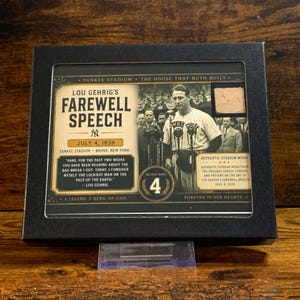 May include: A black framed display featuring a commemorative card for Lou Gehrig's farewell speech on July 4, 1939. The card includes a black and white photograph of Gehrig at a microphone, a piece of authentic stadium wood, and the number 4.