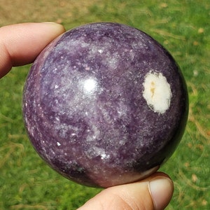 May include: A polished purple and white Lepidolite sphere with a white patch on the surface.