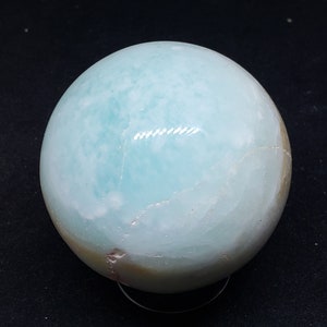 May include: A light blue and white agate sphere with a smooth, polished surface. The sphere is sitting on a clear stand.